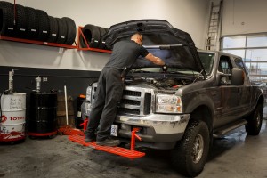 Mechanic on bumper of ford diesel working on engine.
