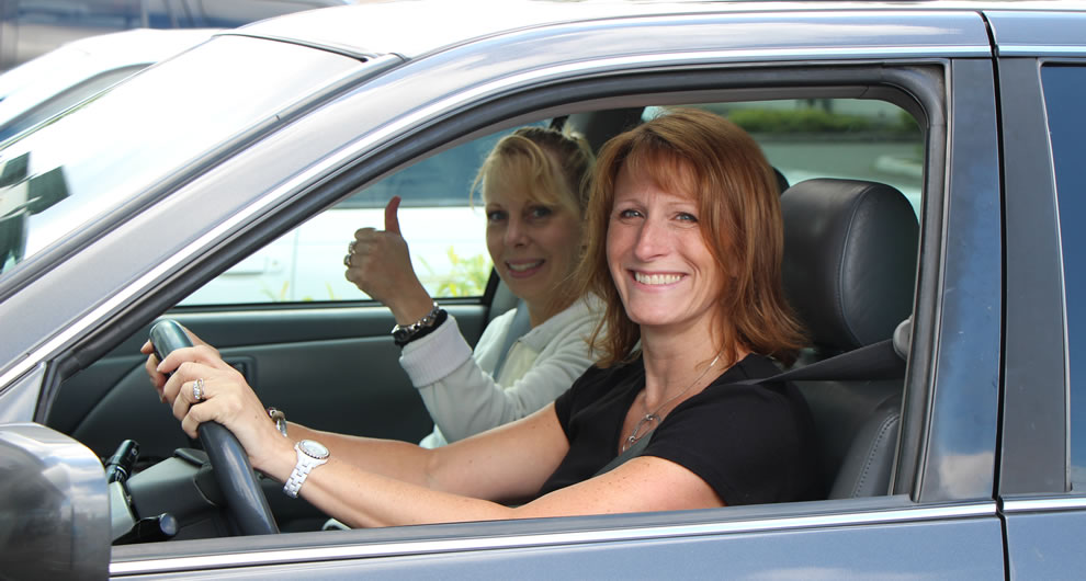 Two ladies smiling in a car thumbs up