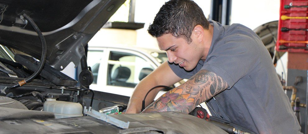 Mechanic smiling with tattooed arm with both arms down into engine working